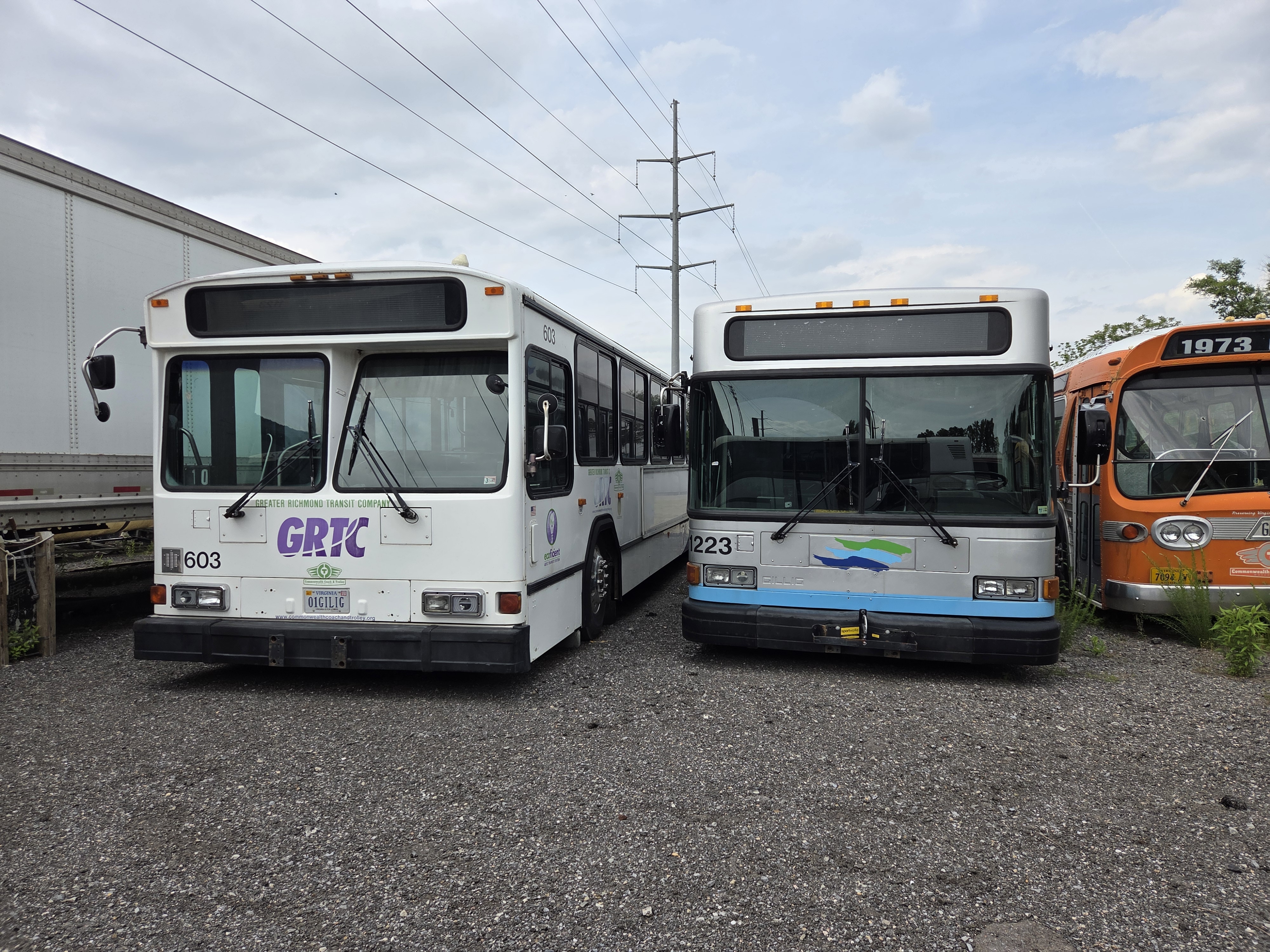 Two buses, a GRTC Gillig Phantom and HRT Gillig Low Floor parked in the museum lot beside an orange GM Fishbowl